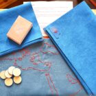 Full layout of the game including a hand-stitched leather map board, wooden tokens, vibrant suede blue pouchs, and playing cards